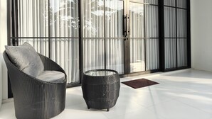 A room with a large sliding glass door, a wicker chair with a cushion, and a small round table. - Alam Cottage Uluwatu (Pecatu)