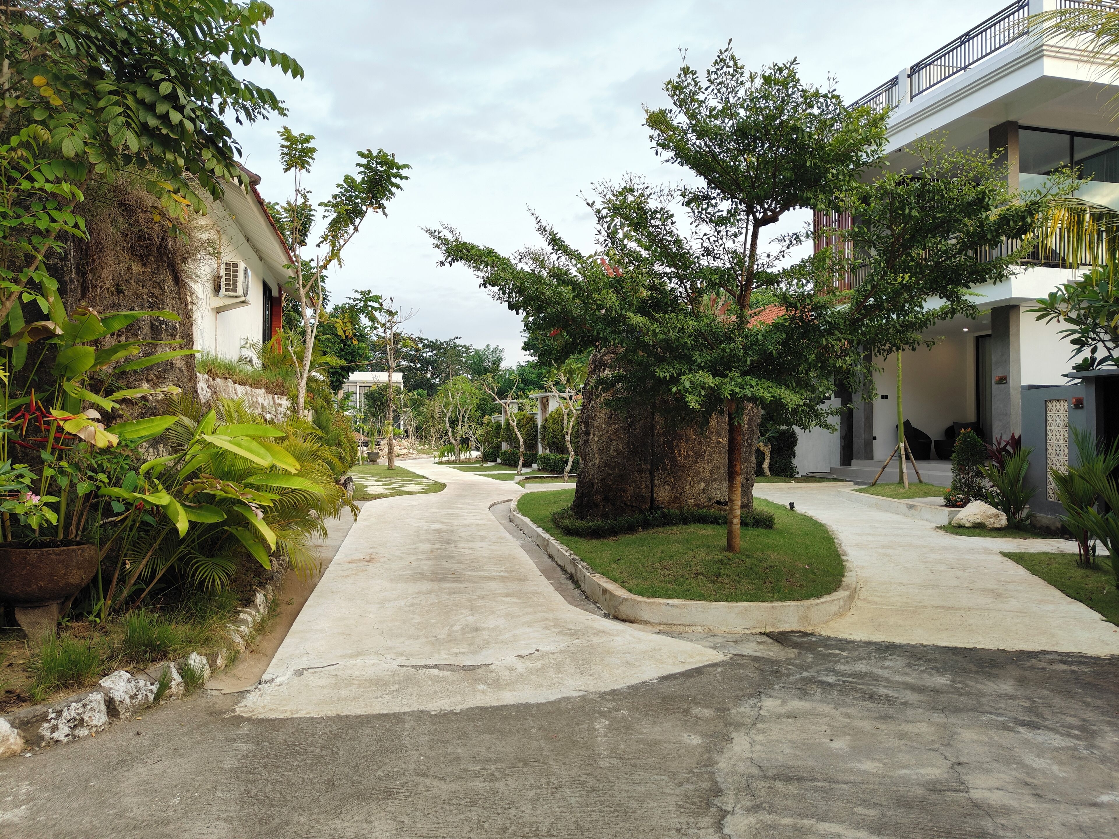 A residential street with houses on both sides, a central grassy area, and a concrete pathway.