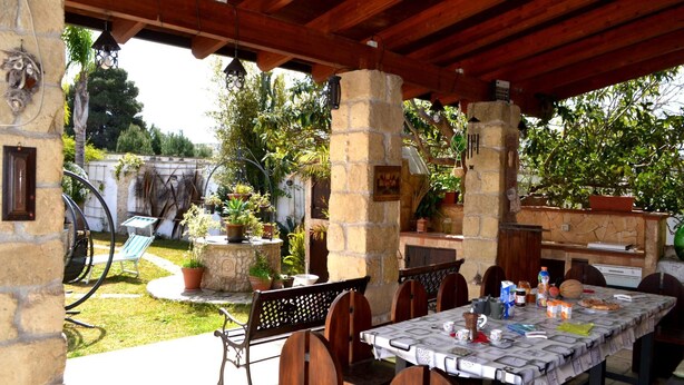 Un patio al aire libre con una mesa lista para comer, rodeado de pilares de piedra y vigas de madera.