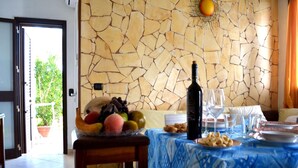 Un comedor con pared de piedra, un frutero, una botella de vino y una mesa preparada para dos.