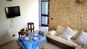 Un comedor con una mesa lista para cuatro personas, un sofá y un televisor montado en la pared.