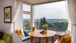 A cozy room with a large window, a round wooden table, and a green sofa.