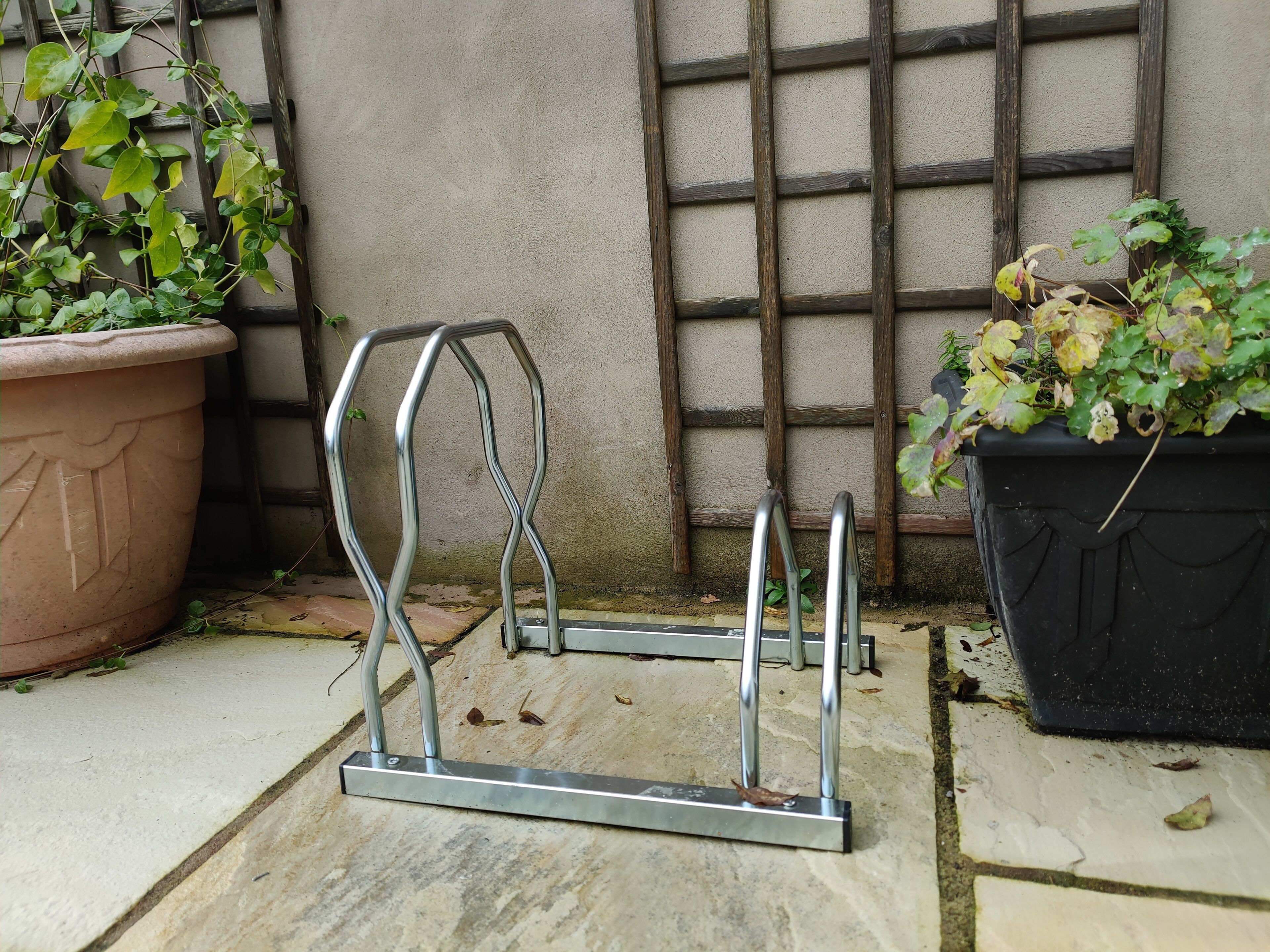 Ein Metallgestell mit einer ebenen Fläche, platziert auf einer gefliesten Terrasse neben einem Blumentopf und einer Holzkonstruktion.
