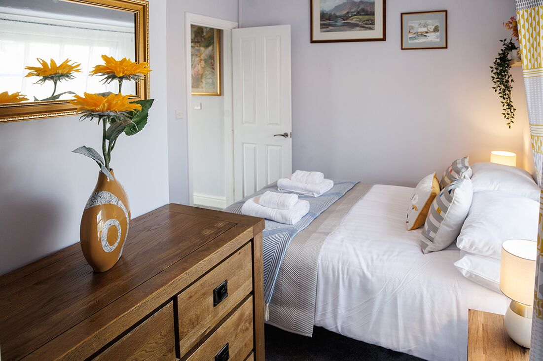 A hotel room with a bed, a dresser, a mirror, and a vase with flowers.