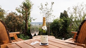 A wooden table with a bottle of wine and two glasses on it, surrounded by greenery.