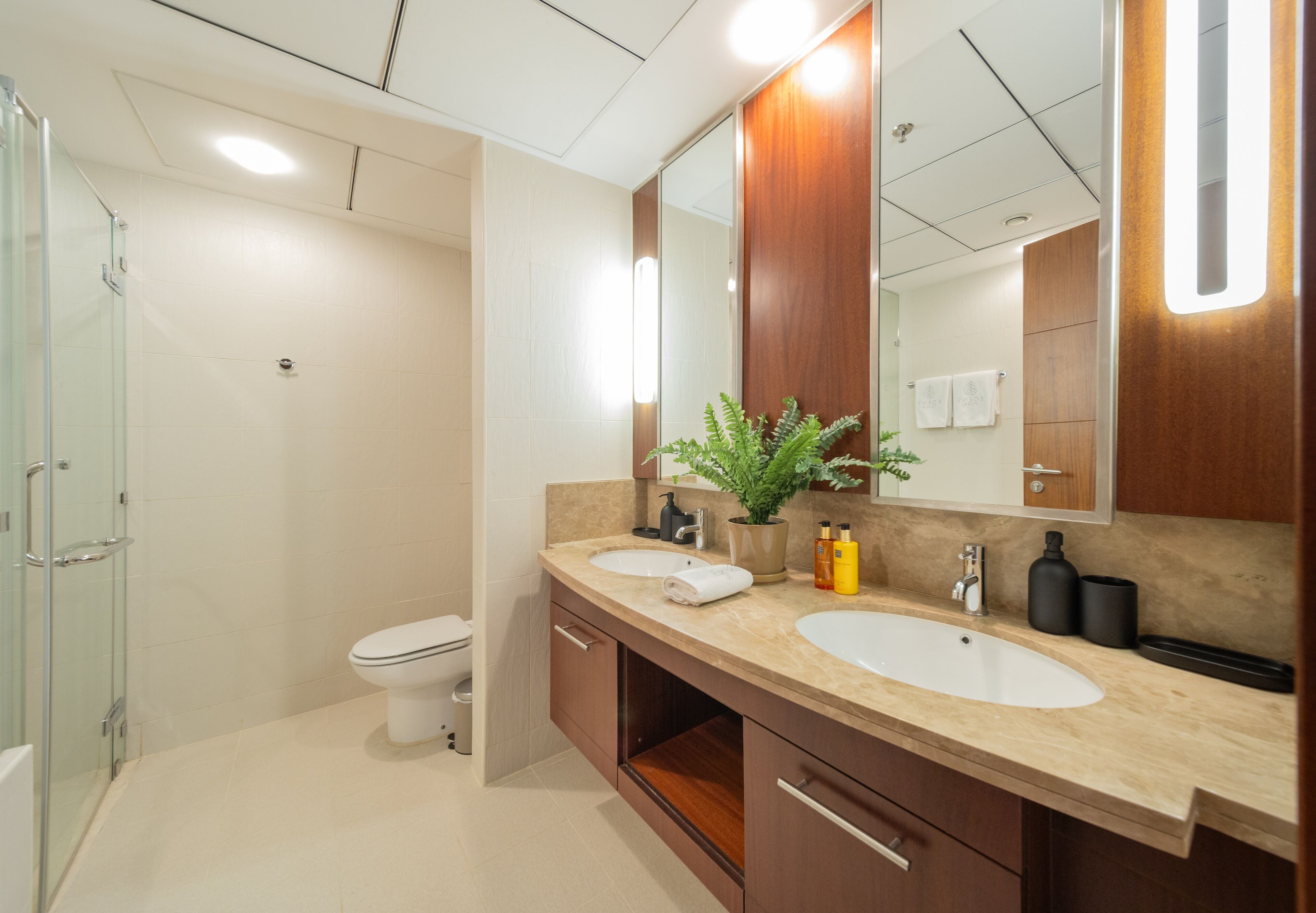A modern bathroom with two sinks, a glass shower enclosure, and a large mirror.