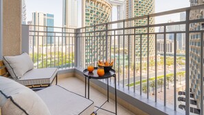 Ein Balkon mit Sofa und Tisch, der einen Blick auf moderne Hochhäuser und eine angelegte Grünfläche bietet.
