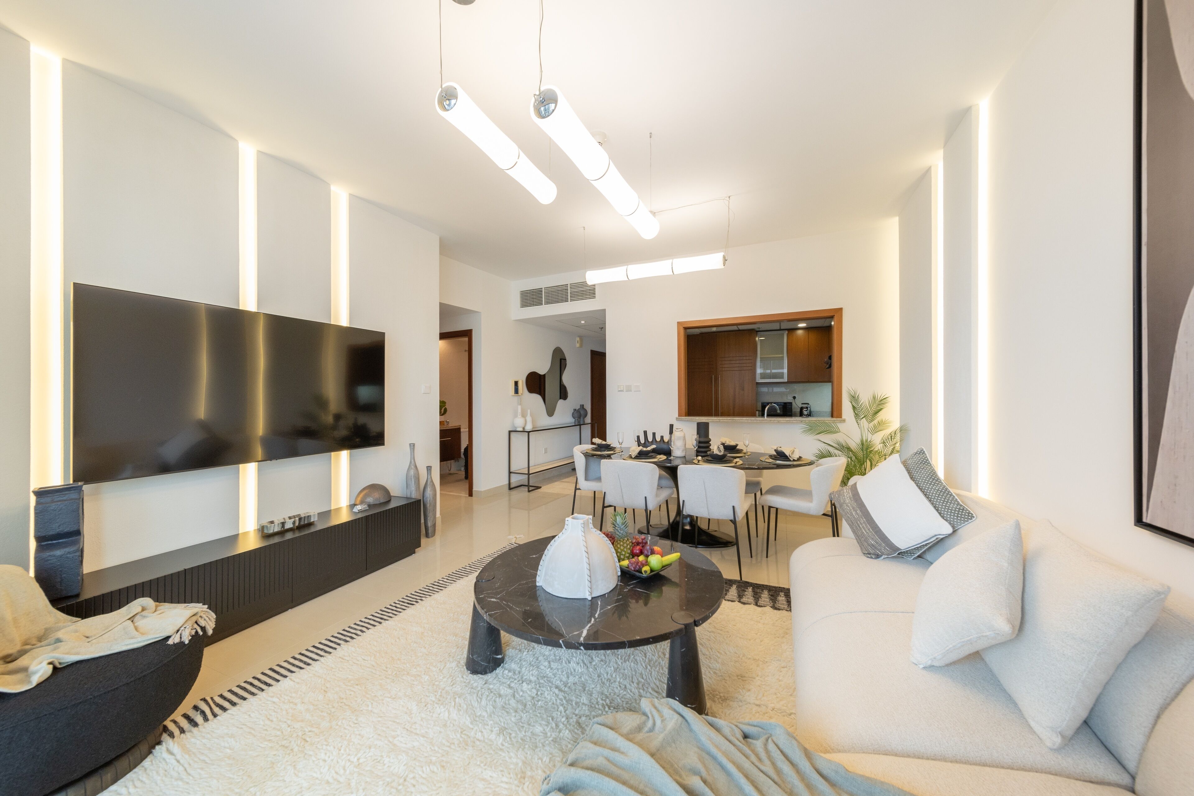 A modern living room with a flat-screen TV, a dining area, and a kitchen.