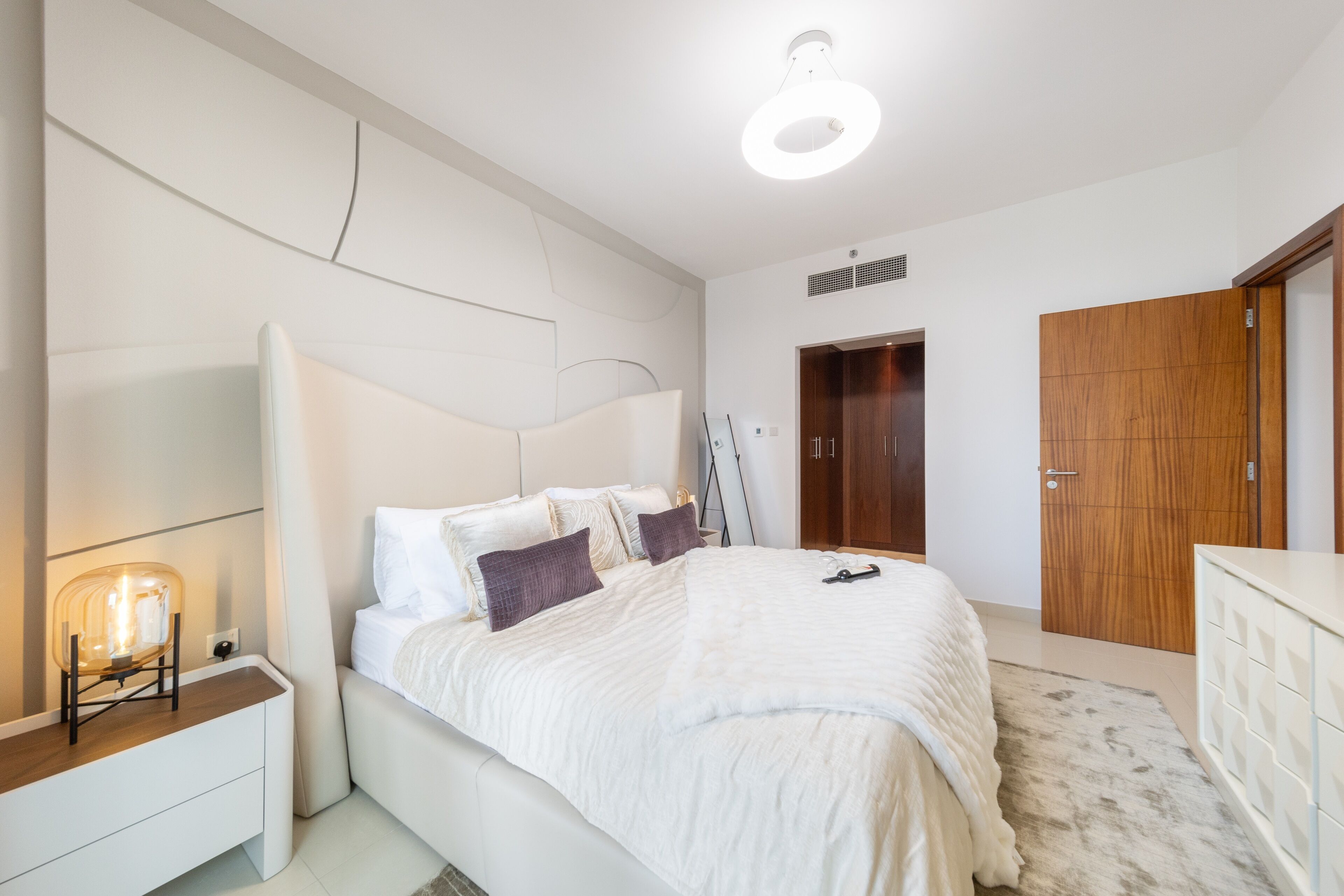 A modern bedroom with a large bed, a bedside table, a wardrobe, and a ceiling light.