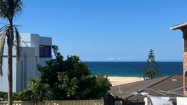 Une propriété située en bord de mer, dotée d’un bâtiment moderne, d’une plage de sable et offrant une vue dégagée sur l’océan.