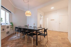 Un comedor con una mesa y sillas negras, un colgante de luz y un piso de madera con patrón de espiga.