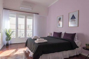 Un dormitorio con una cama, una planta en maceta, una ventana con cortinas y dos cuadros en la pared.
