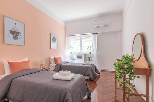 Une chambre d’hôtel avec deux lits, un grand miroir, une plante en pot et une fenêtre avec des rideaux.