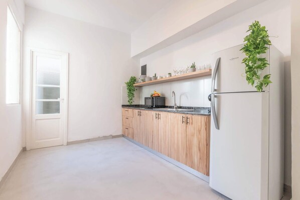 Una cocina moderna con armarios blancos, encimera negra y refrigerador blanco. Hay plantas en la encimera y una ventana a la izquierda.