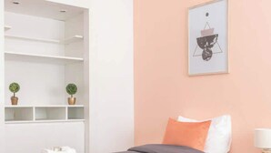 Een slaapkamer met twee bedden, een witte garderobe, een plank met planten en een lijst met een foto aan de muur.