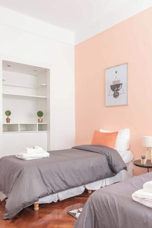A bedroom with two beds, a white wardrobe, a shelf with plants, and a framed picture on the wall.