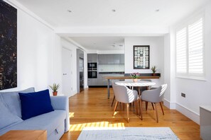 Ein modernes Wohnzimmer mit einer Couch, einem Esstisch mit Stühlen und einer Küche im Hintergrund.