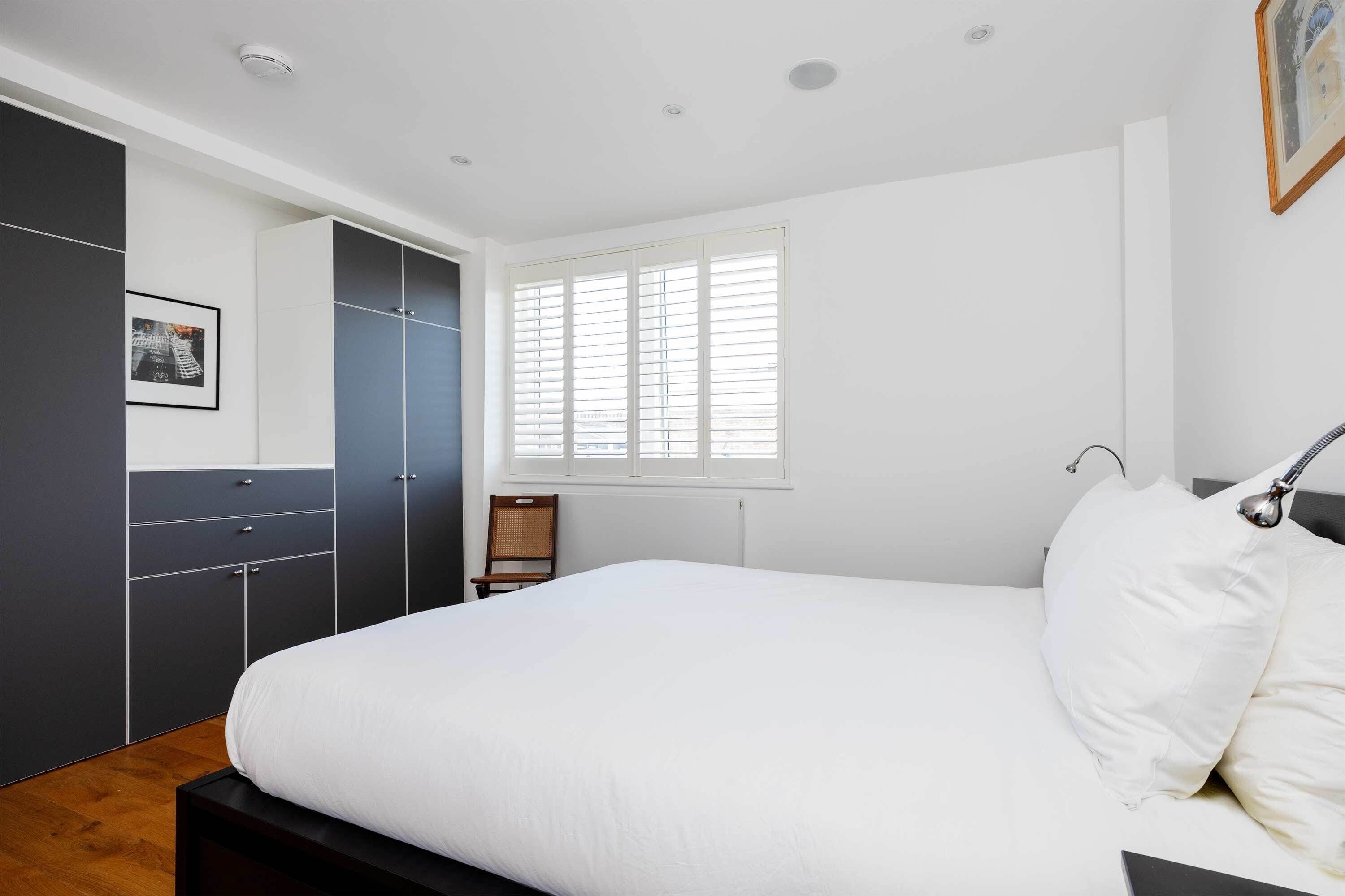Een slaapkamer met een groot bed, een kledingkast, een stoel en een raam met zonwering.