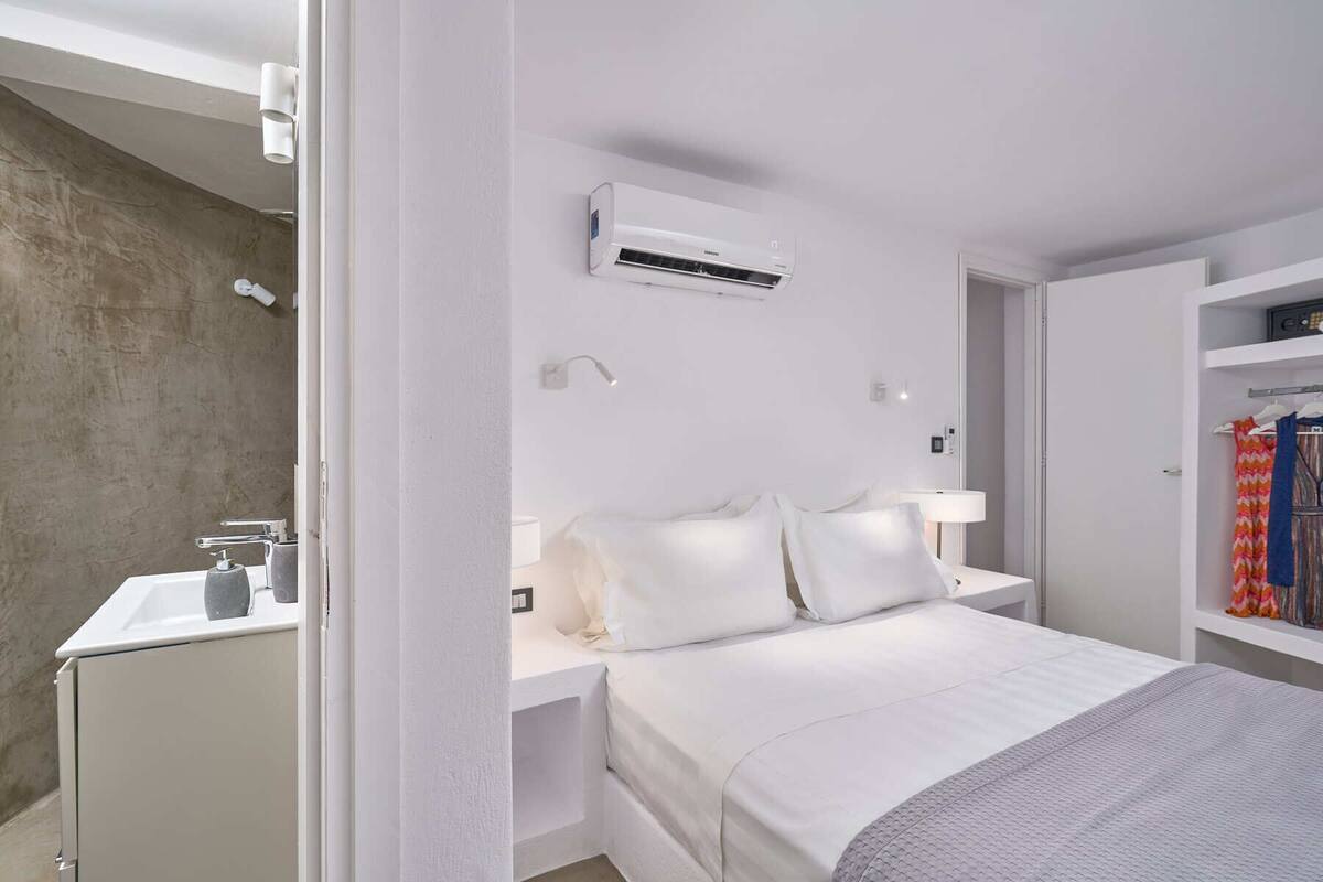 A modern hotel room with a bed, bedside table, and an air conditioning unit.