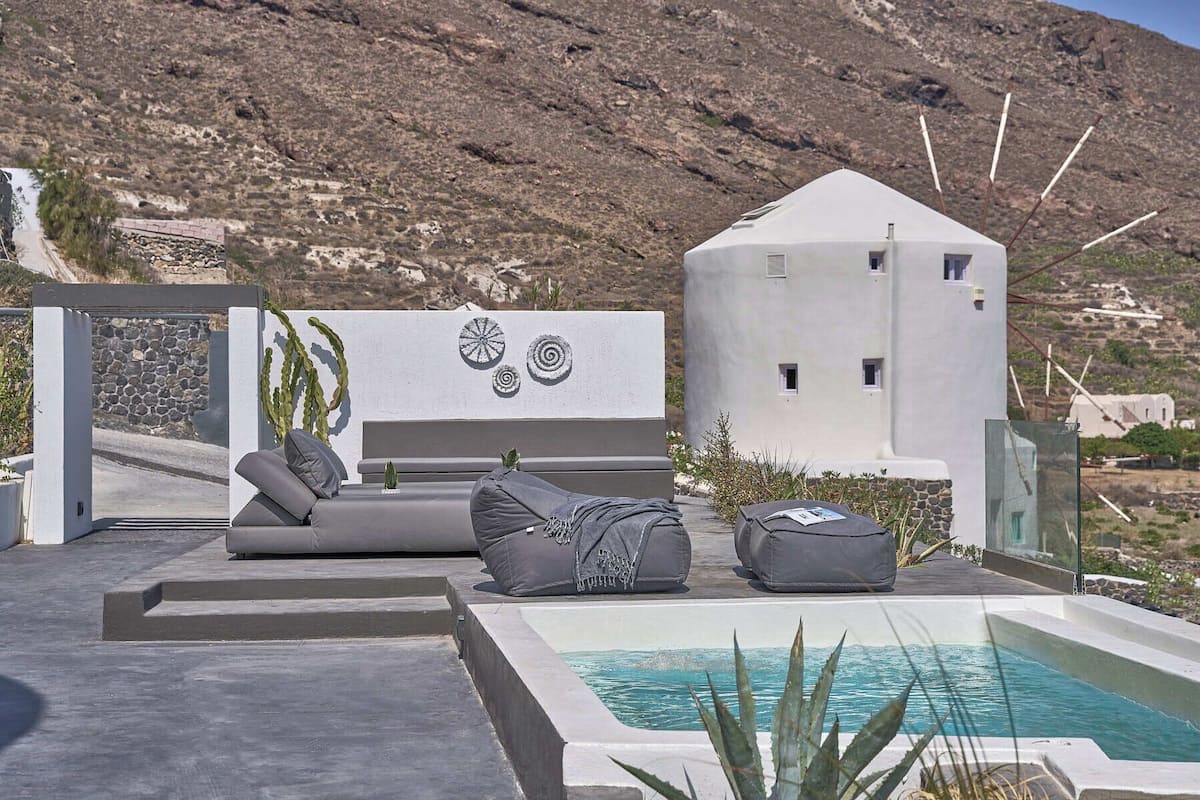 A modern outdoor seating area with a pool, featuring a minimalist design with a white building and a mountainous backdrop.