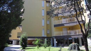 A multi-story building with balconies, a covered entrance, and a parking area. - Lovely Flat at Grado Pineta (Grado)