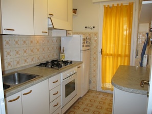 A kitchen with white cabinets, a gas stove, a sink, and a yellow curtain.