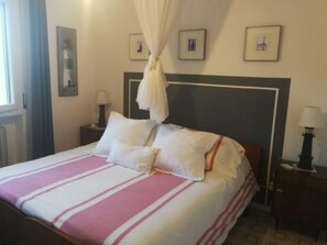 Une chambre d’hôtel avec un lit, deux tables de chevet, une fenêtre avec des rideaux et des tableaux encadrés au mur.