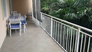 A balcony with a table and chairs, surrounded by a white railing and lush greenery. - Lovely Flat at Grado Pineta (Grado)
