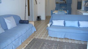 A living room with two blue sofas, a patterned rug, and a dining area with a table and chairs. - Lovely Flat at Grado Pineta (Grado)