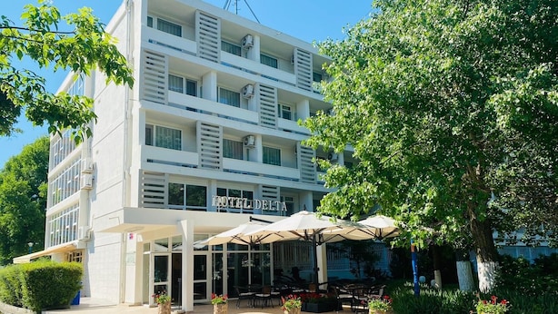 A hotel with a white facade, multiple balconies, and outdoor seating with umbrellas. - HOTEL DELTA (Constanta)