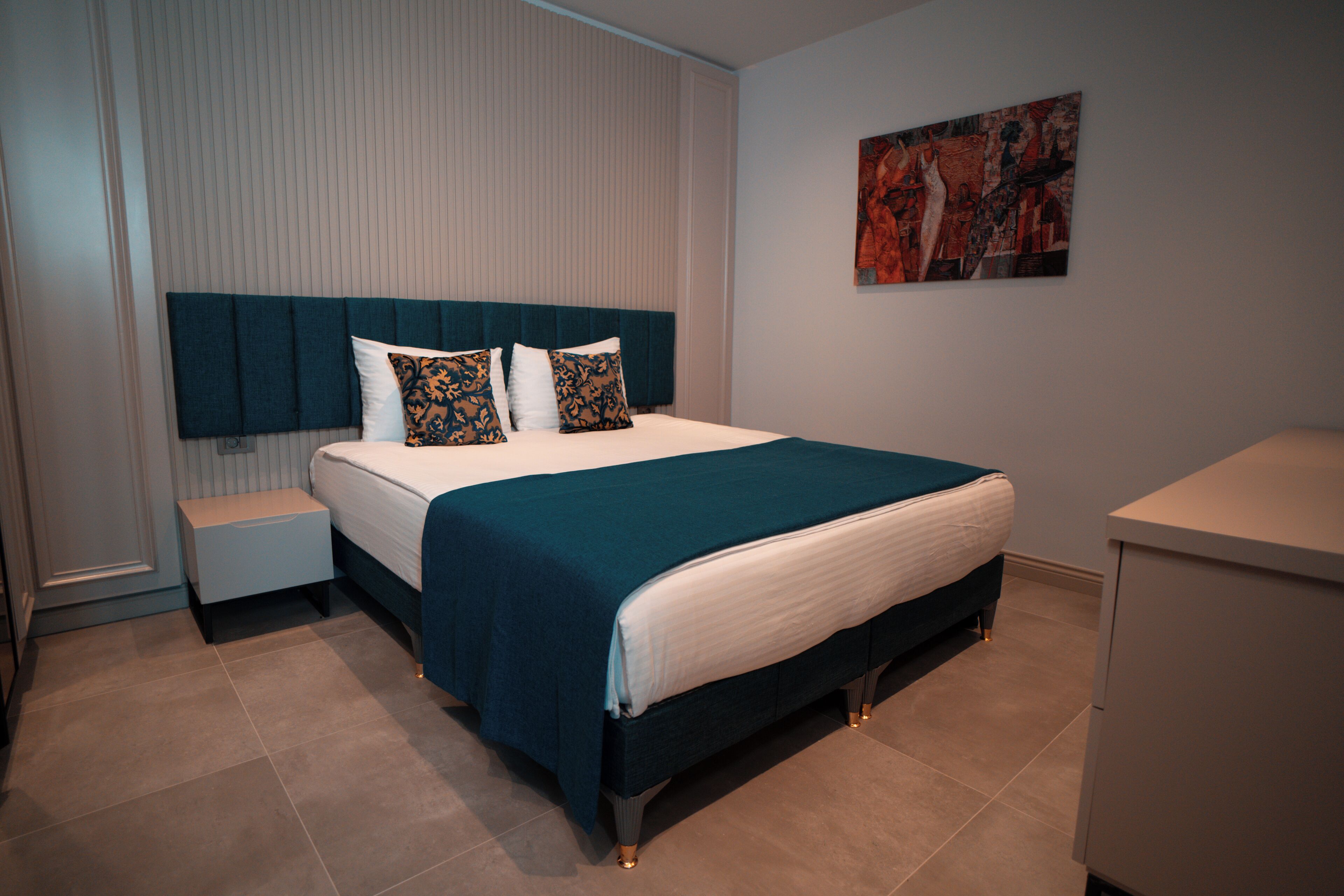 A modern bedroom with a large bed, a bedside table, a nightstand, and a wall-mounted artwork.