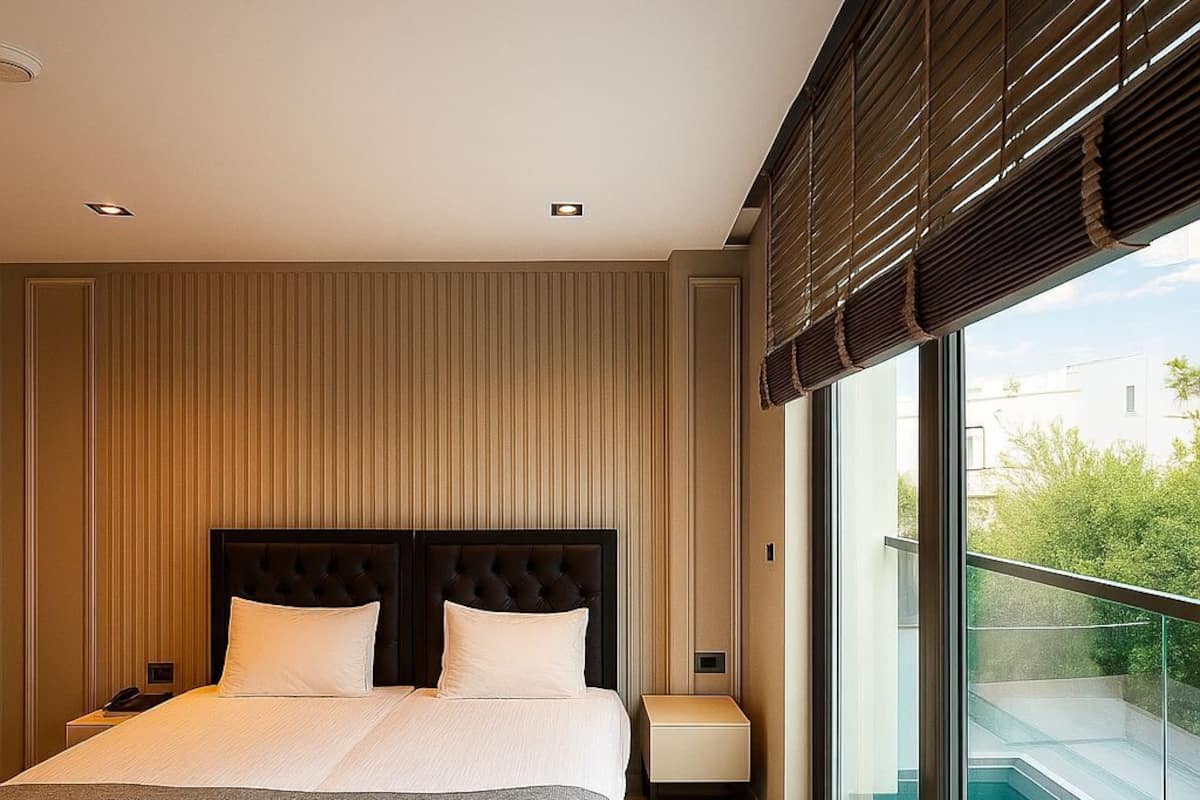 A modern bedroom with a large bed, a nightstand, a bedside table, and a view of a swimming pool through large windows.