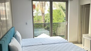 Une chambre moderne avec un grand lit, un téléphone sur la table de chevet et une vue sur la verdure grâce à une porte-fenêtre coulissante.