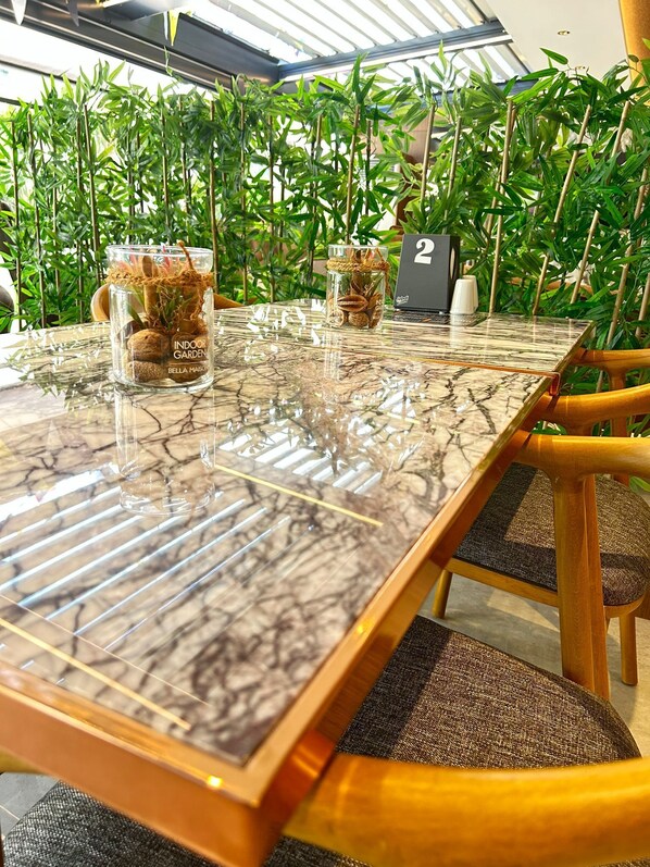 A glass-top table with two glass vases containing plants, set in a room with bamboo plants in the background.