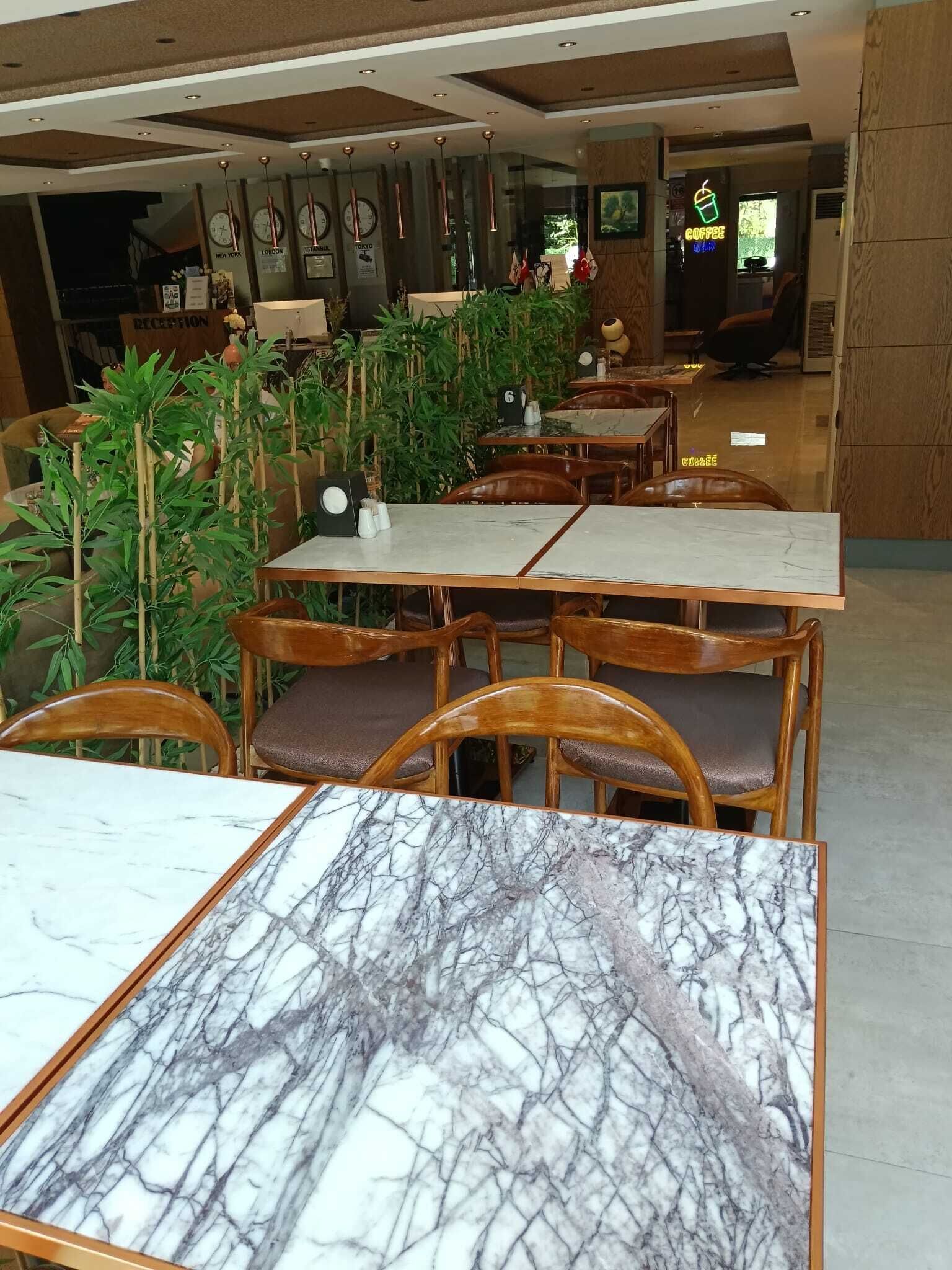 A restaurant with marble-topped tables and wooden chairs, a reception area with clocks, and a neon coffee sign.