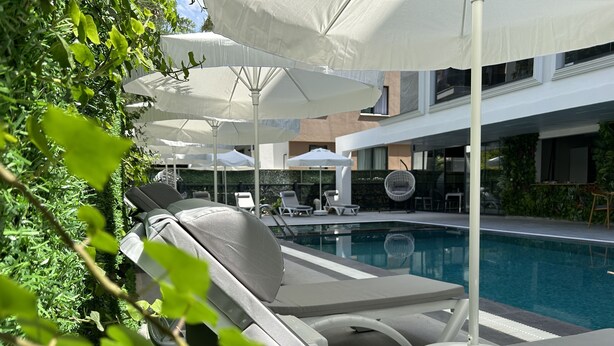 Un espace aménagé au bord de la piscine, avec des chaises longues et des parasols, une piscine, et un bâtiment moderne en arrière-plan.