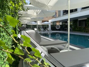 A poolside area with lounge chairs and umbrellas, a pool, and a modern building in the background.