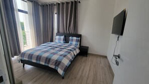 Une chambre à coucher avec un lit, des rideaux, un téléviseur fixé au mur et un plancher en bois.