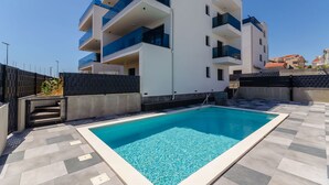 Un moderno edificio de apartamentos con piscina, balcones y zona de patio con baldosas.