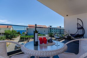 A balcony with wicker furniture, a table with a bottle and candles, and a view of buildings and greenery.