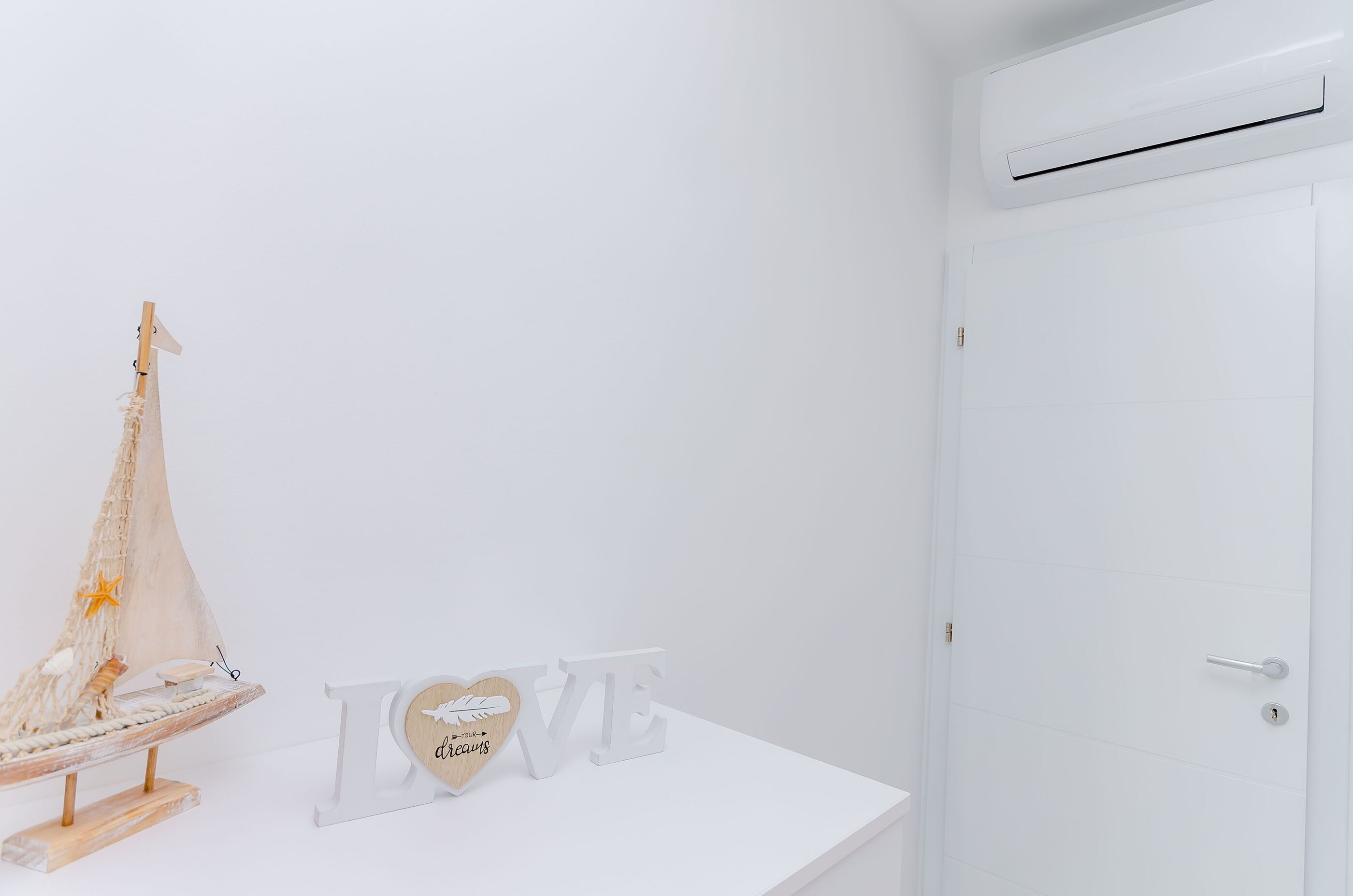 A white room with a wooden sailboat decoration, a white wall, and a white door.