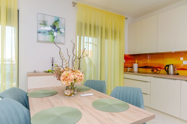A modern kitchen with a yellow curtain, a vase with flowers, and a painting on the wall.
