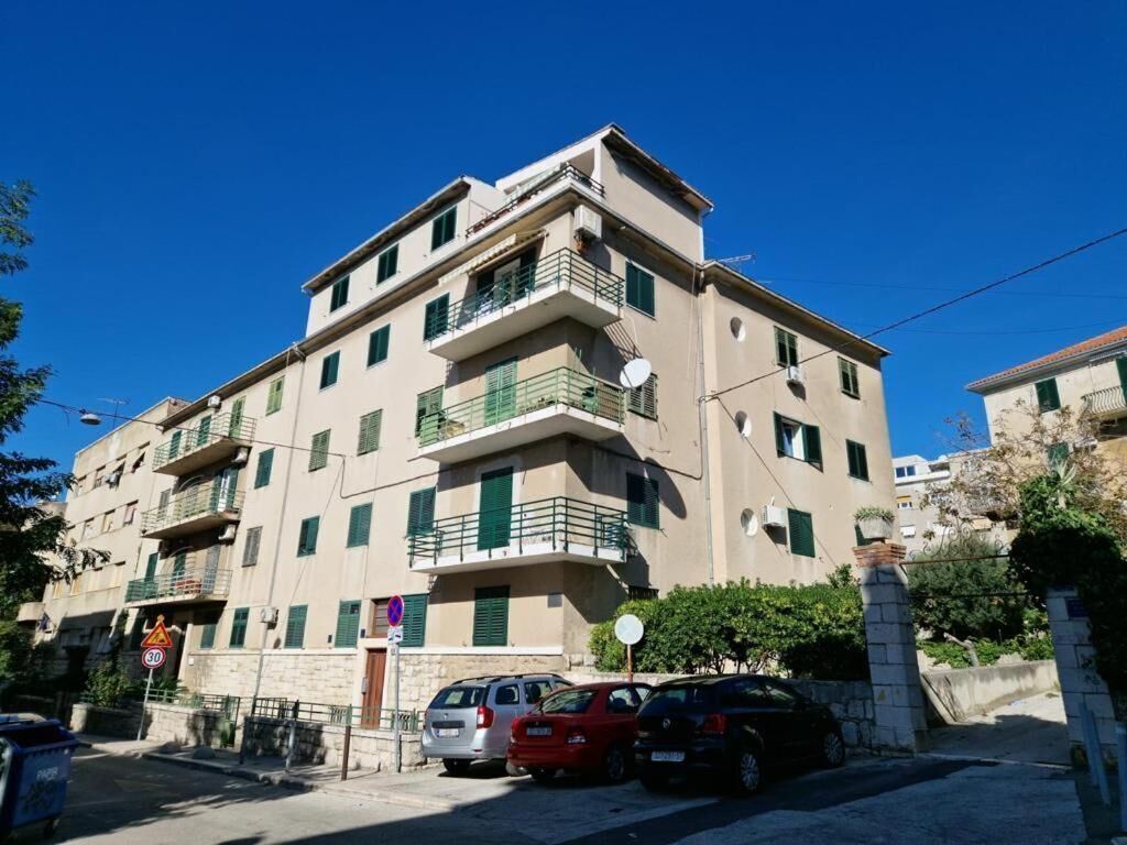 A multi-story residential building with balconies, a street sign indicating a 30 km/h speed limit, and parked cars.