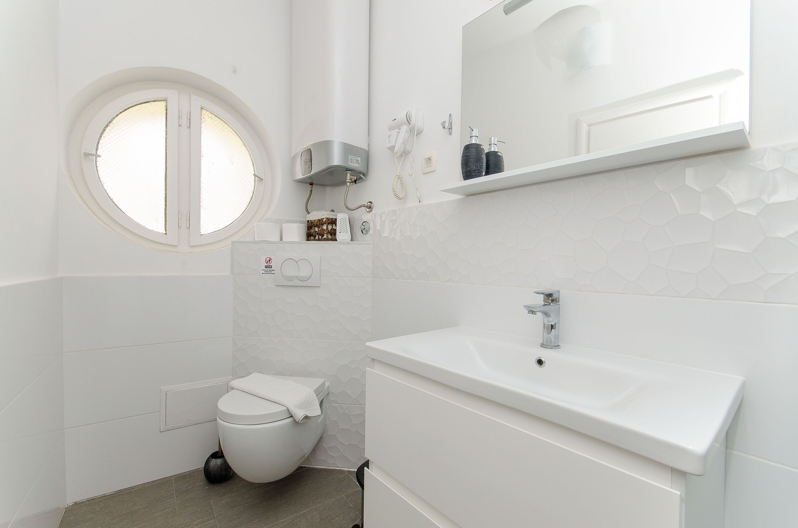 Un bagno moderno con il water, un lavandino e una finestra rotonda.