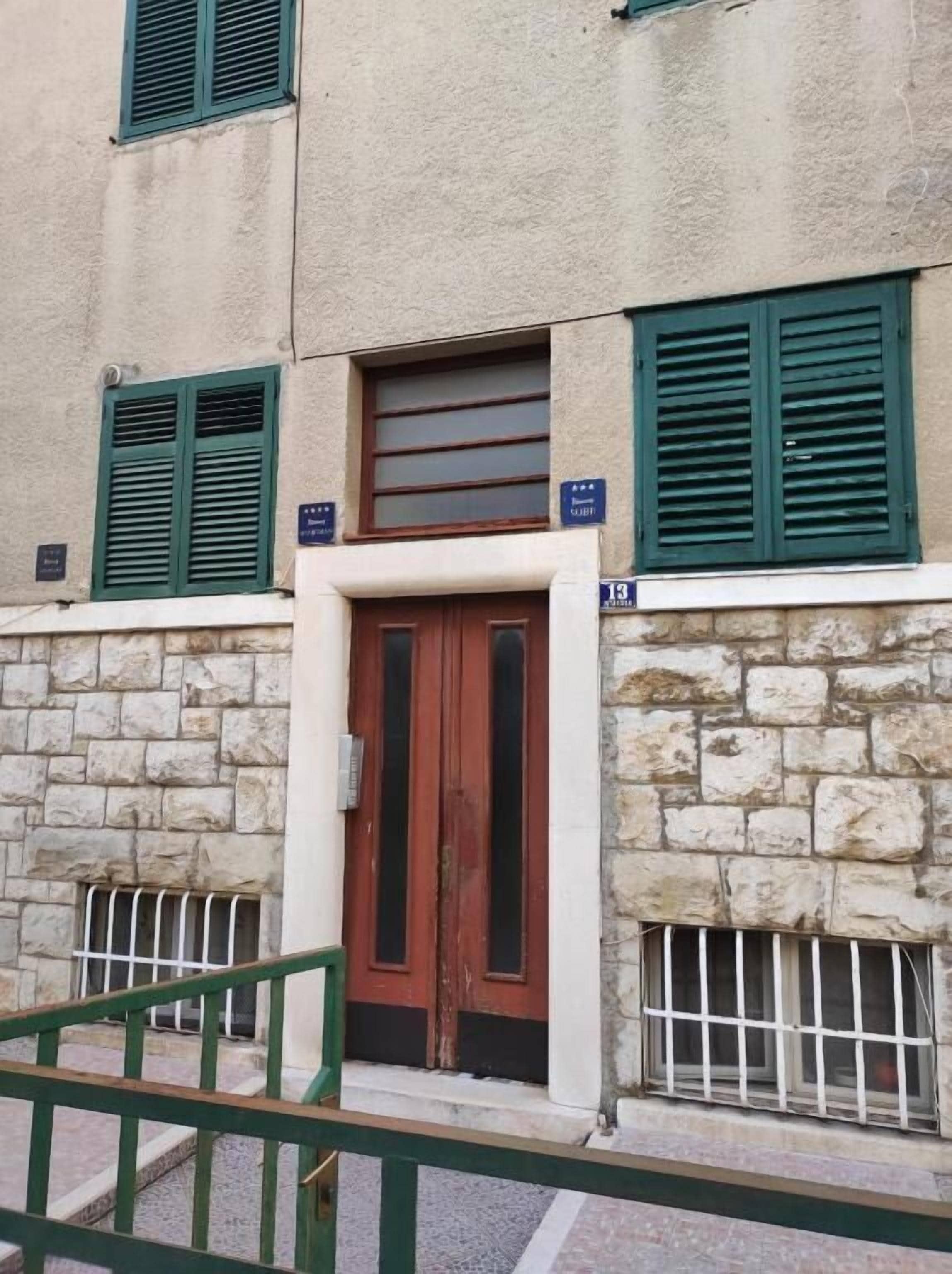 Un edificio de fachada de piedra, puerta de madera y contraventanas verdes.