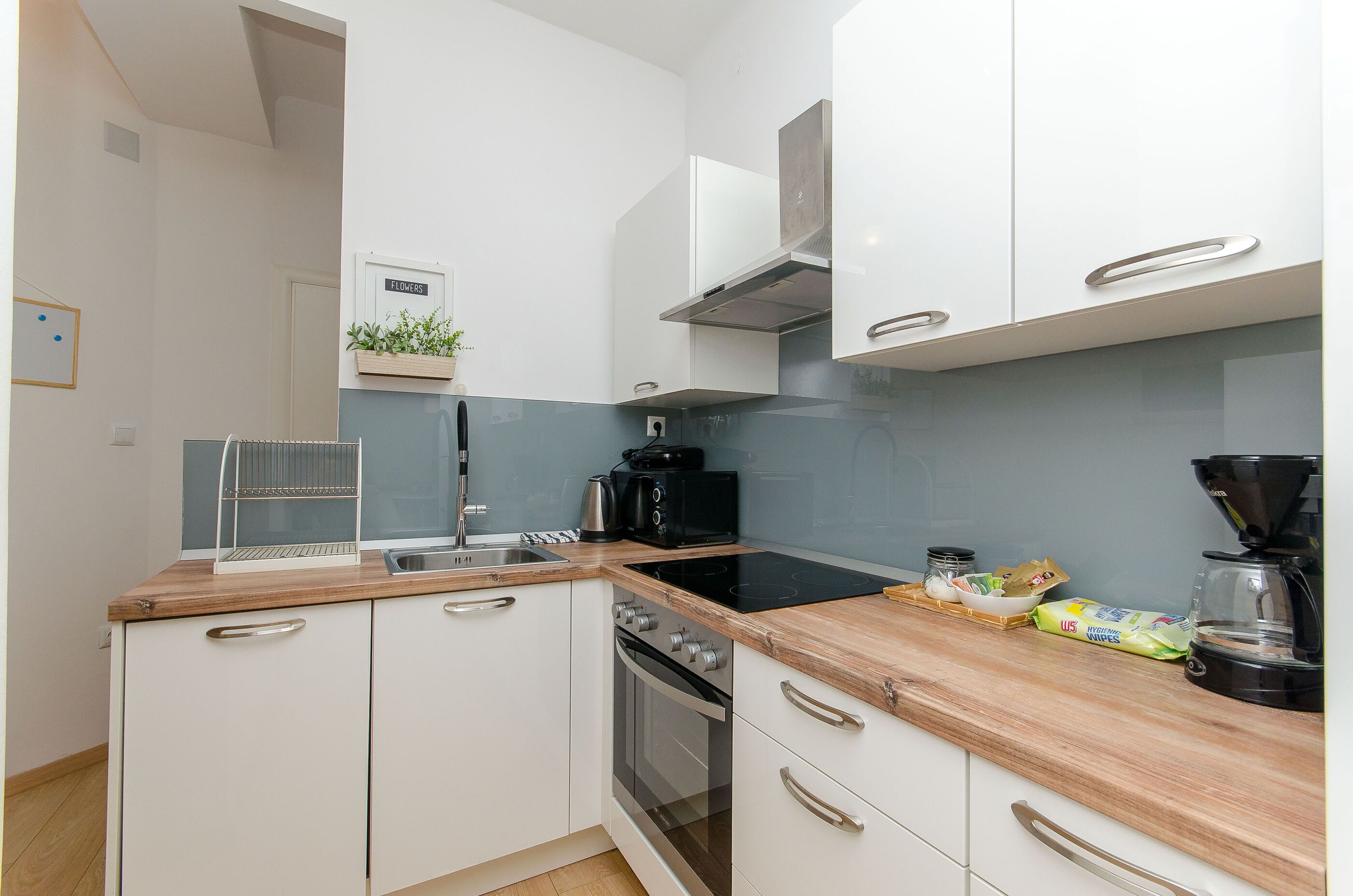 Una cocina moderna con armarios blancos, encimera de madera, horno integrado, microondas y cafetera.