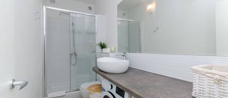A modern bathroom with a glass shower enclosure, a white sink, and a built-in washing machine.
