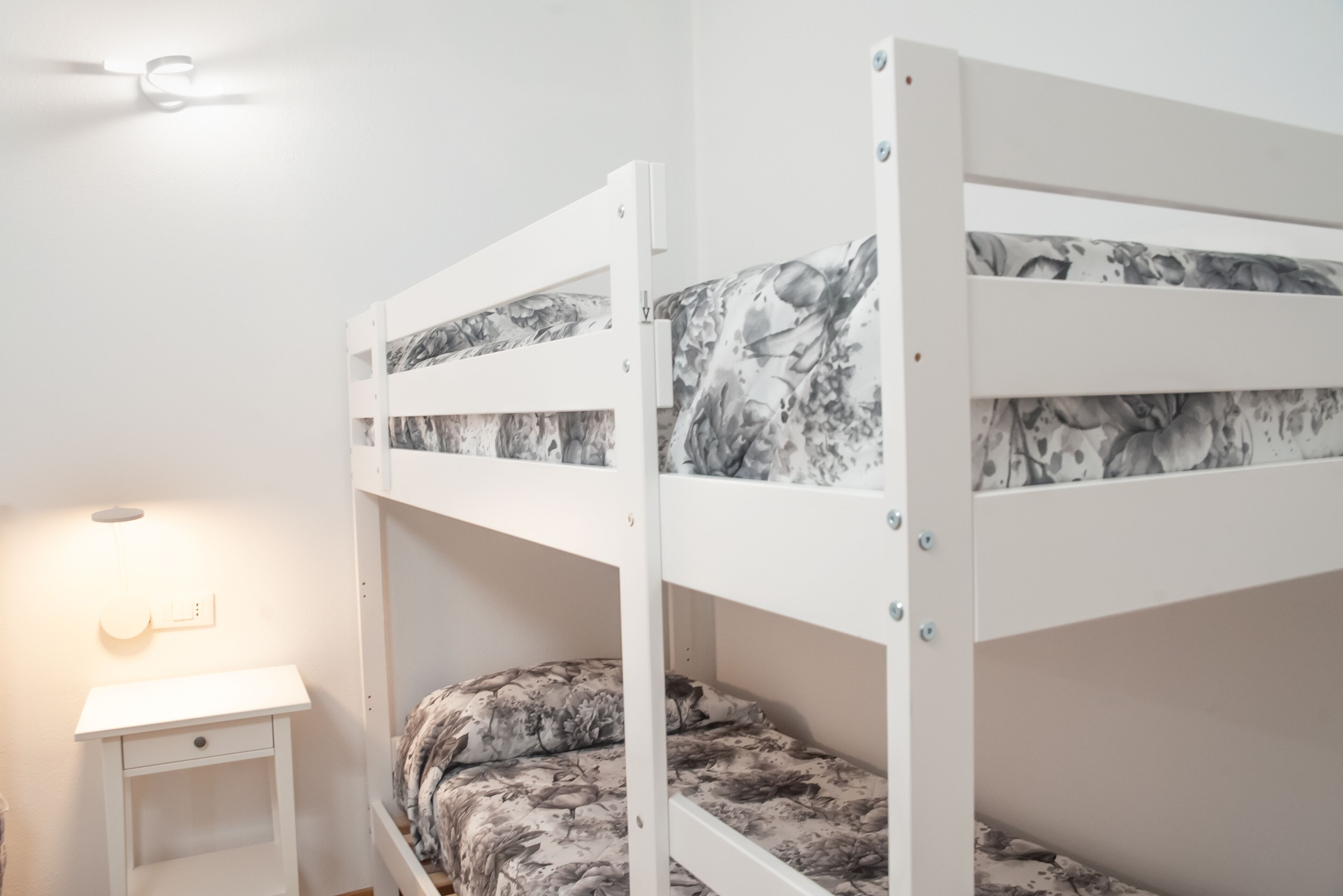 Ein Schlafraum mit Etagenbetten, einer weißen Wand, einem kleinen Nachttisch und einer Wandleuchte.