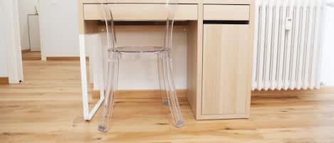 A wooden desk with a clear chair in a room with wooden flooring.