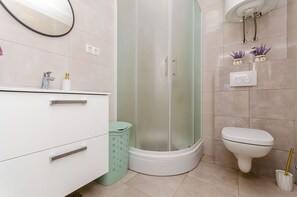 A modern bathroom with a glass-enclosed shower, a toilet, and a vanity with drawers. - Apartment Rizza (Trogir)